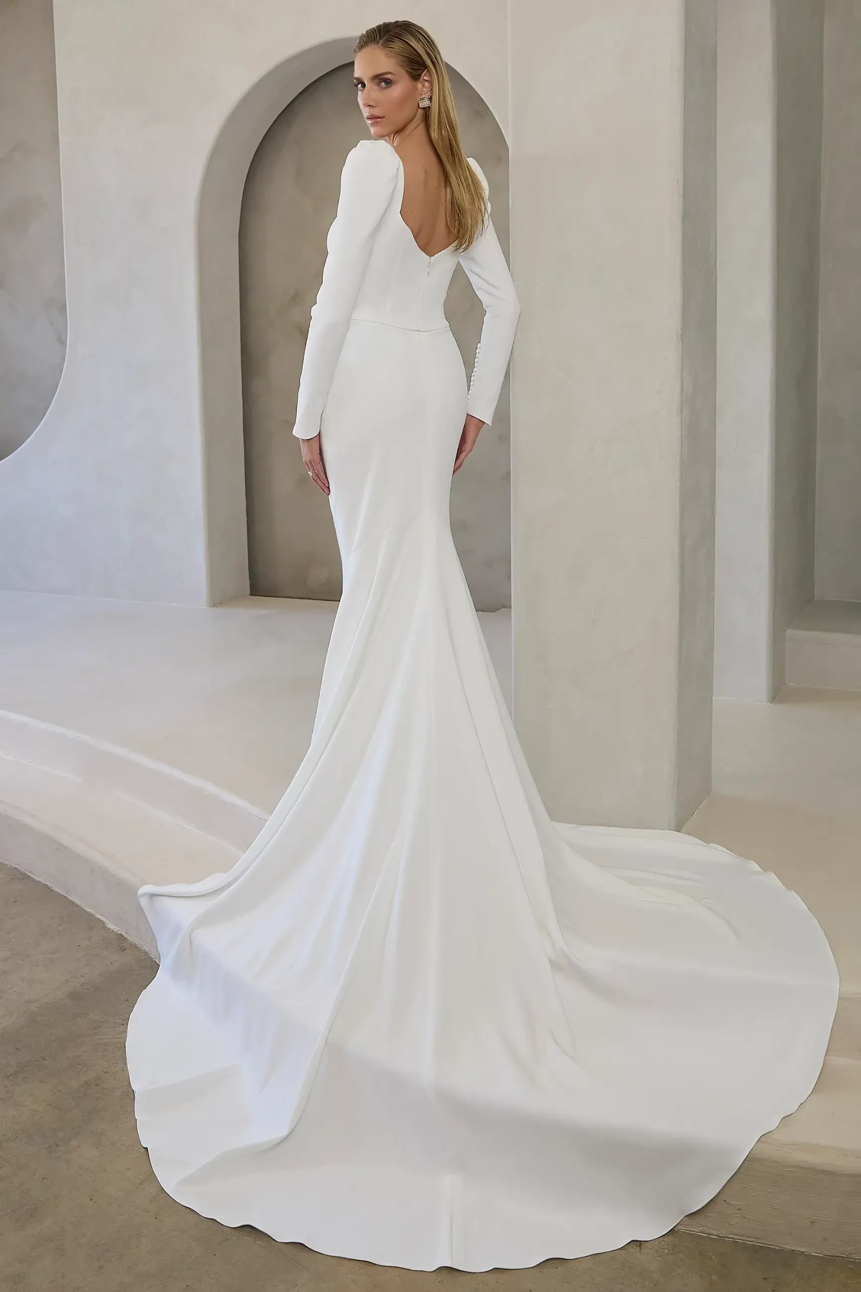 Model is wearing Noa, a fit-and-flare gown with a sweetheart neckline, long gathered sleeves with covered buttons, a subtle v-back, and a dramatic 76-inch train.